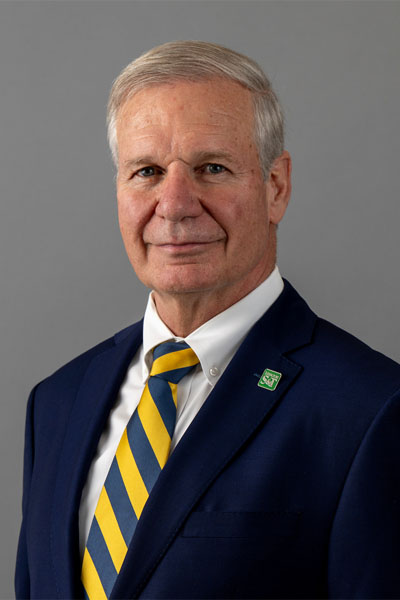 Portrait of a man with short hair, velvet navy blue blazer, white colored shirt, and a striped gold and navy tie.